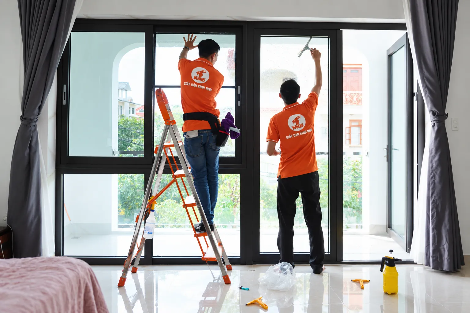 Hai kỹ thuật viên NND vệ sinh hệ cửa kính lớn trước khi dán phim cách nhiệt AP7080 tại biệt thự Vinhomes Riverside