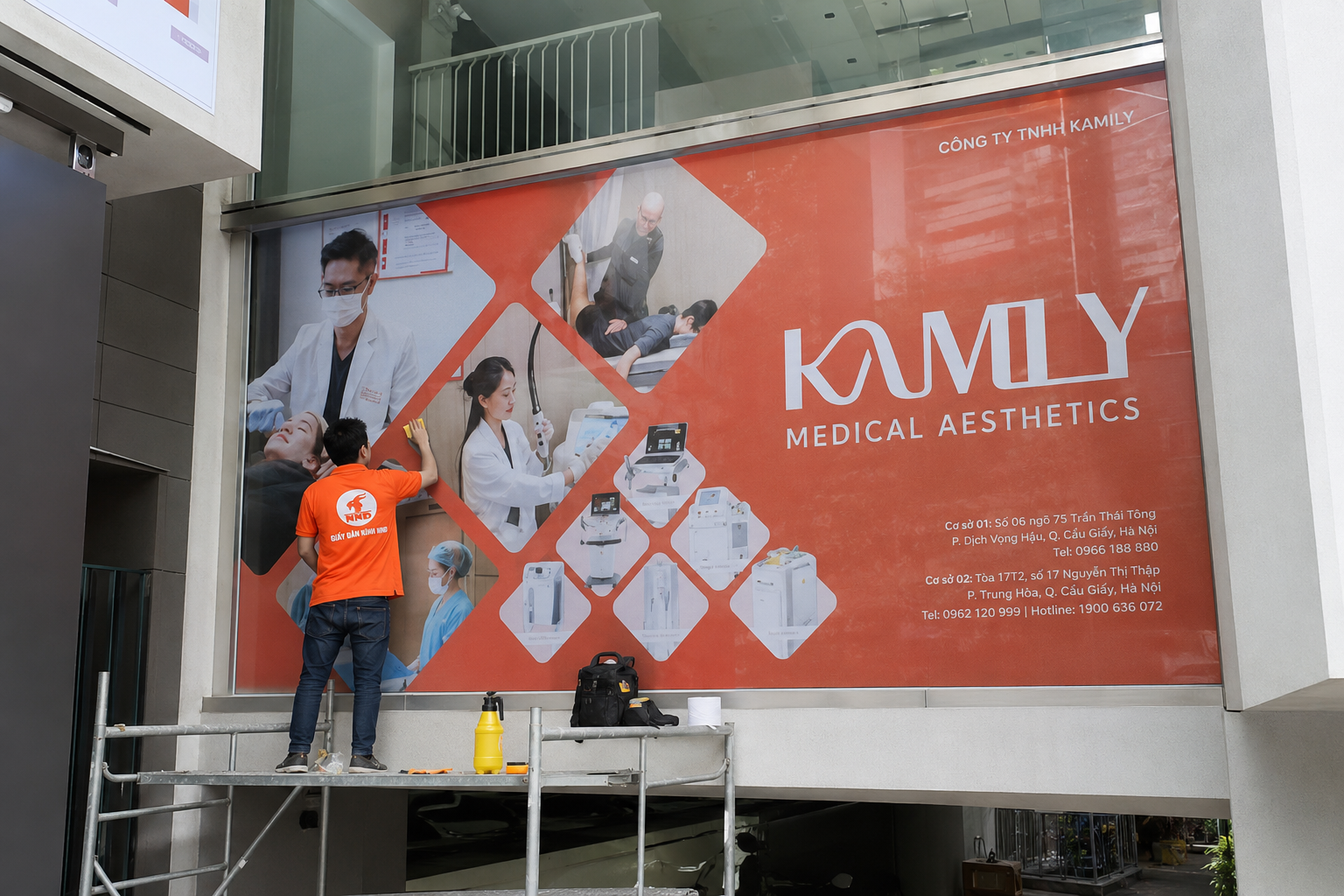 Thợ NND dán decal quảng cáo cho viện thẩm mỹ Kamly trên mặt kính lớn