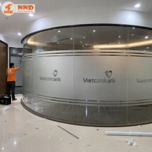 Thiết kế decal mờ cắt logo âm bản Vietcombank bo tròn mềm mại theo hệ vách kính cong phòng họp, tôn vinh thương hiệu tinh tế và định hình không gian giao dịch cực kỳ chuyên nghiệp, an tâm.