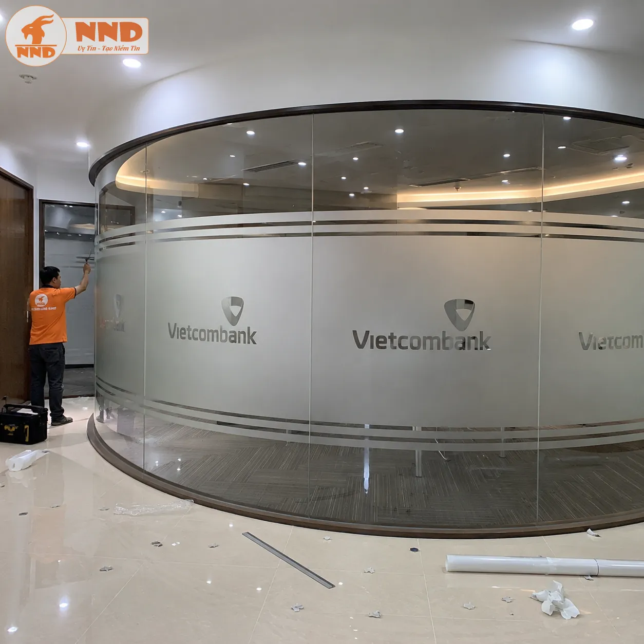 Thiết kế decal mờ cắt logo âm bản Vietcombank bo tròn mềm mại theo hệ vách kính cong phòng họp, tôn vinh thương hiệu tinh tế và định hình không gian giao dịch cực kỳ chuyên nghiệp, an tâm.