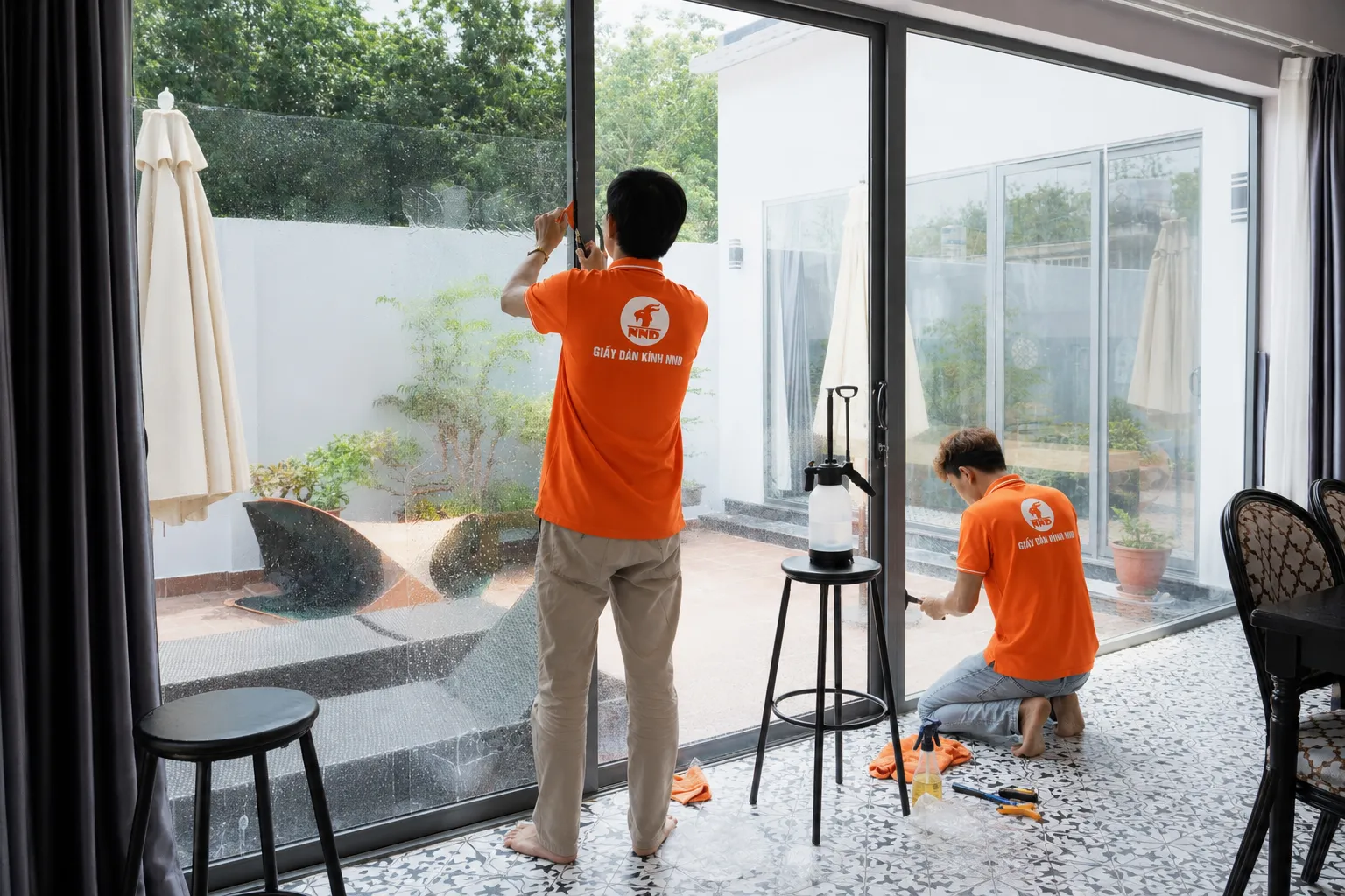 Hai kỹ thuật viên NND thi công phim cách nhiệt trên hệ cửa kính lớn tại nhà ở.