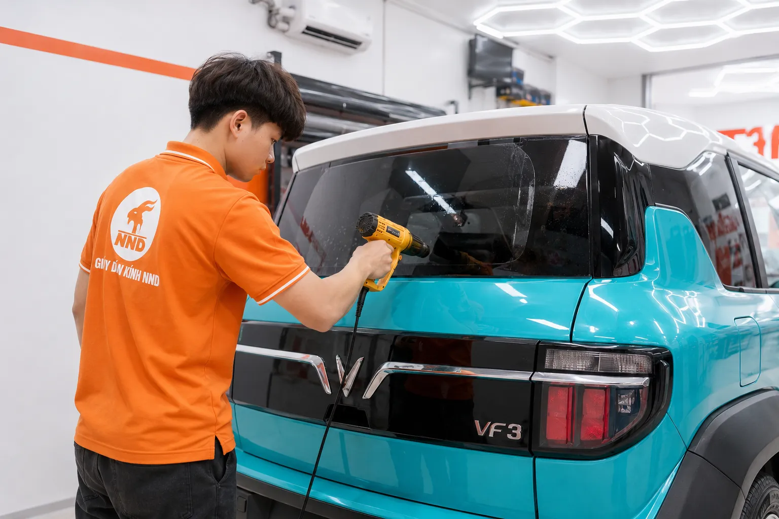 Kỹ thuật viên sử dụng súng nhiệt hoàn thiện phim cách nhiệt kính hậu xe VF3 tại NND