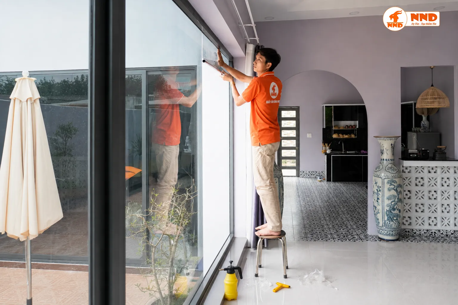Kỹ thuật viên NND dán phim cách nhiệt trên hệ cửa kính cao trong nhà ở.