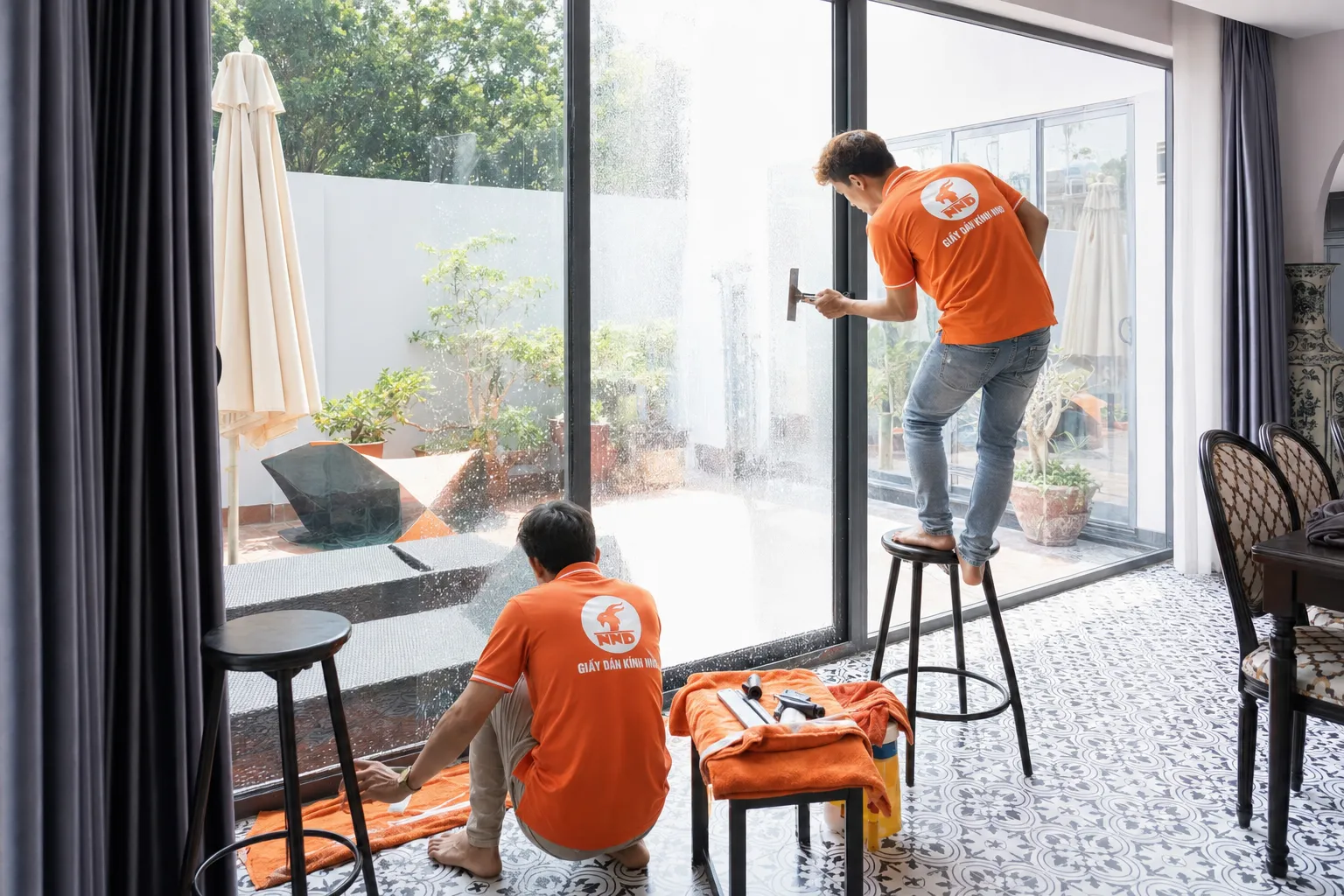 Kỹ thuật viên NND thi công phim cách nhiệt trên cửa kính lớn bằng dụng cụ gạt chuyên dụng.
