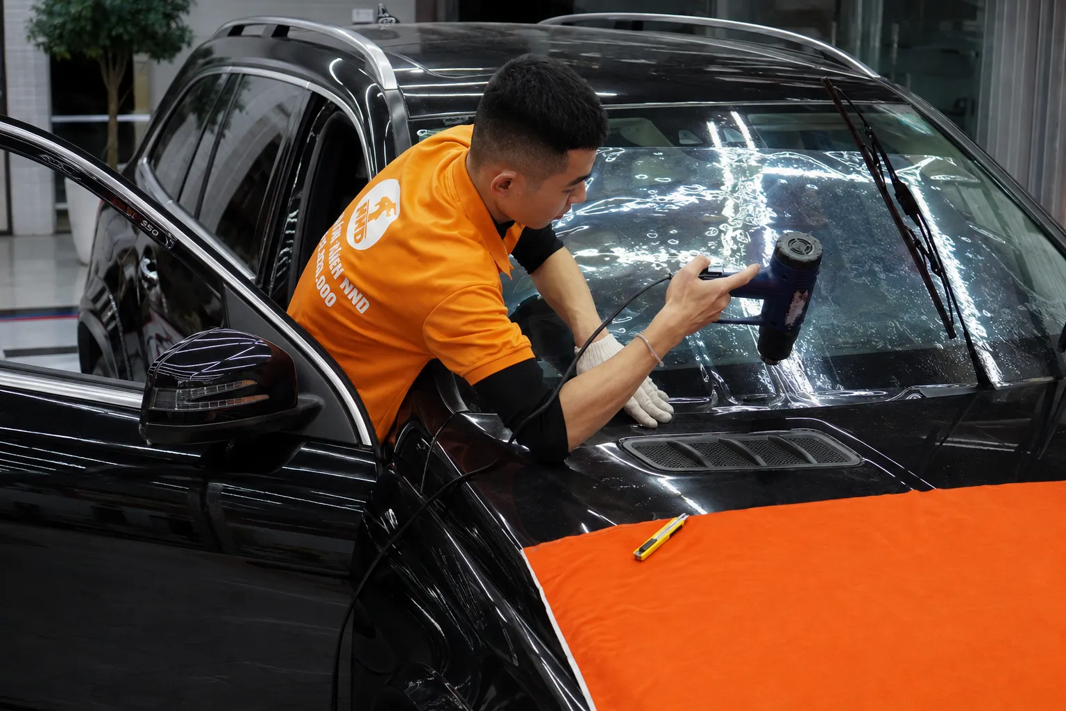 Kỹ thuật viên NND dùng súng nhiệt thi công và định hình phim cách nhiệt trên kính lái ô tô Mercedes.