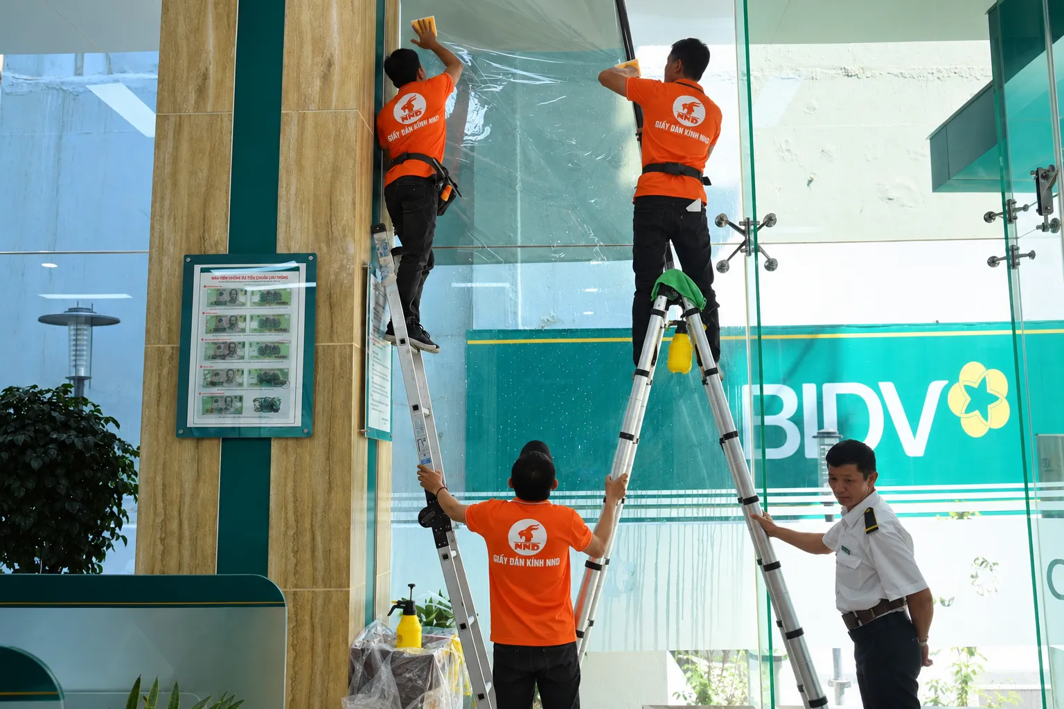 Đội thợ NND thi công dán phim cách nhiệt trên mảng kính lớn văn phòng BIDV
