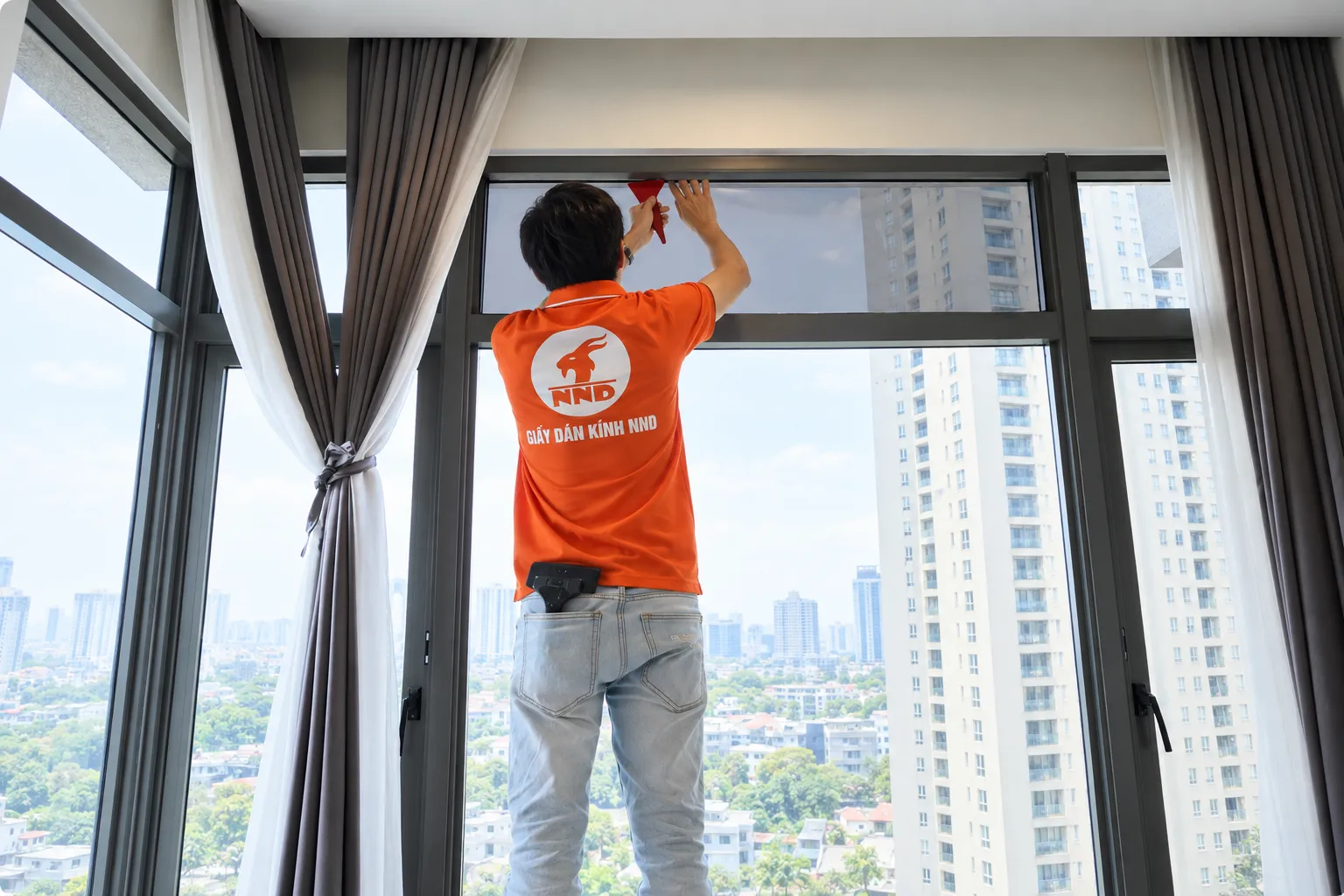 Kỹ thuật viên NND xử lý phim cách nhiệt trên ô kính phía trên tại căn hộ Vinhomes Royal City