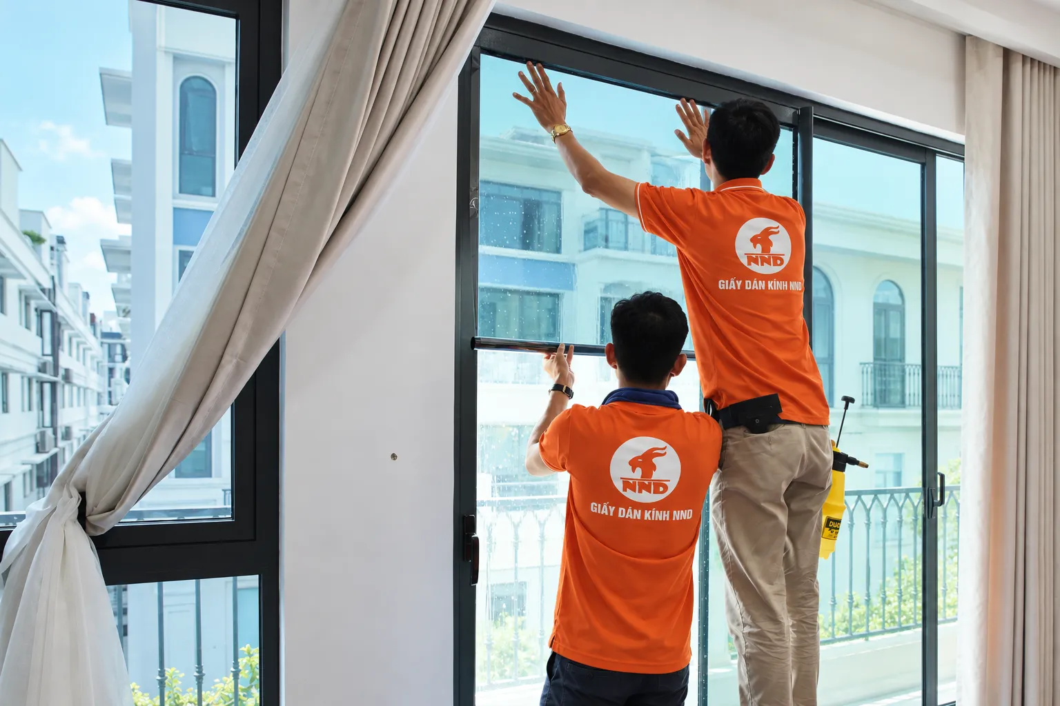 Hai kỹ thuật viên NND thi công phim cách nhiệt trên hệ cửa kính lớn tại Vinhomes Marina