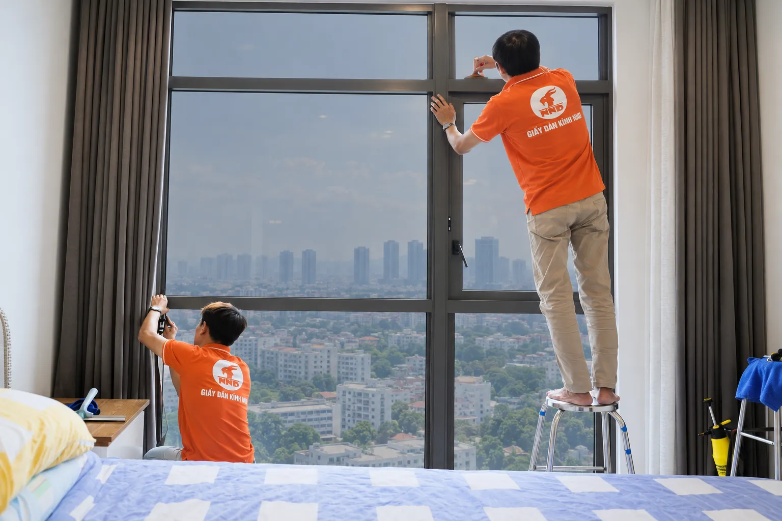 Hai kỹ thuật viên NND kiểm tra và hoàn thiện mép phim cách nhiệt trên hệ kính căn hộ Vinhomes Royal City