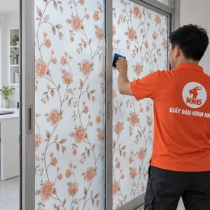 Thợ NND dùng gạt xanh hoàn thiện decal A55 hoa cam nhạt trên vách kính cửa lùa